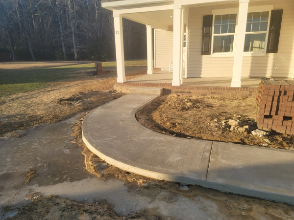 Newly poured concrete walkway curving to the porch of a light-colored house.