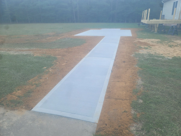 A gray concrete pathway leading to a T-shaped landing in a grassy yard.