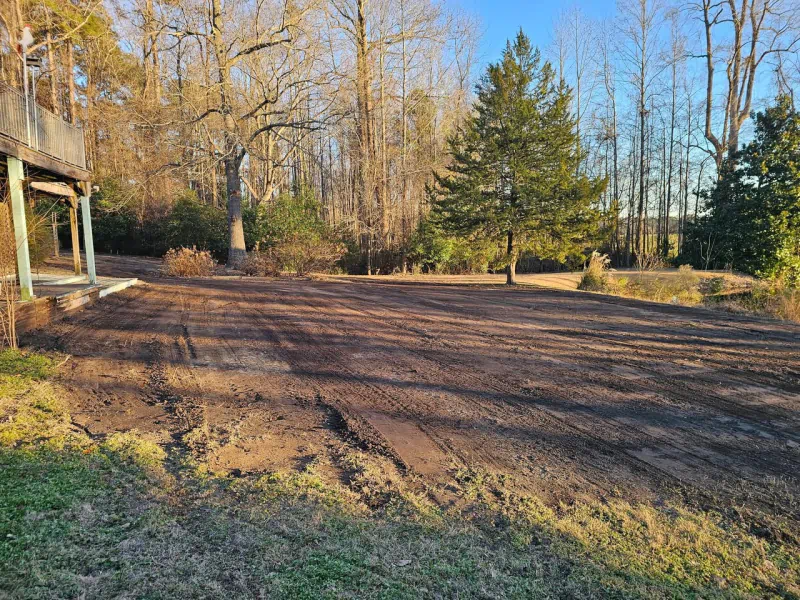 Cleared dirt area with tire tracks, trees in the background, and a porch on the left.