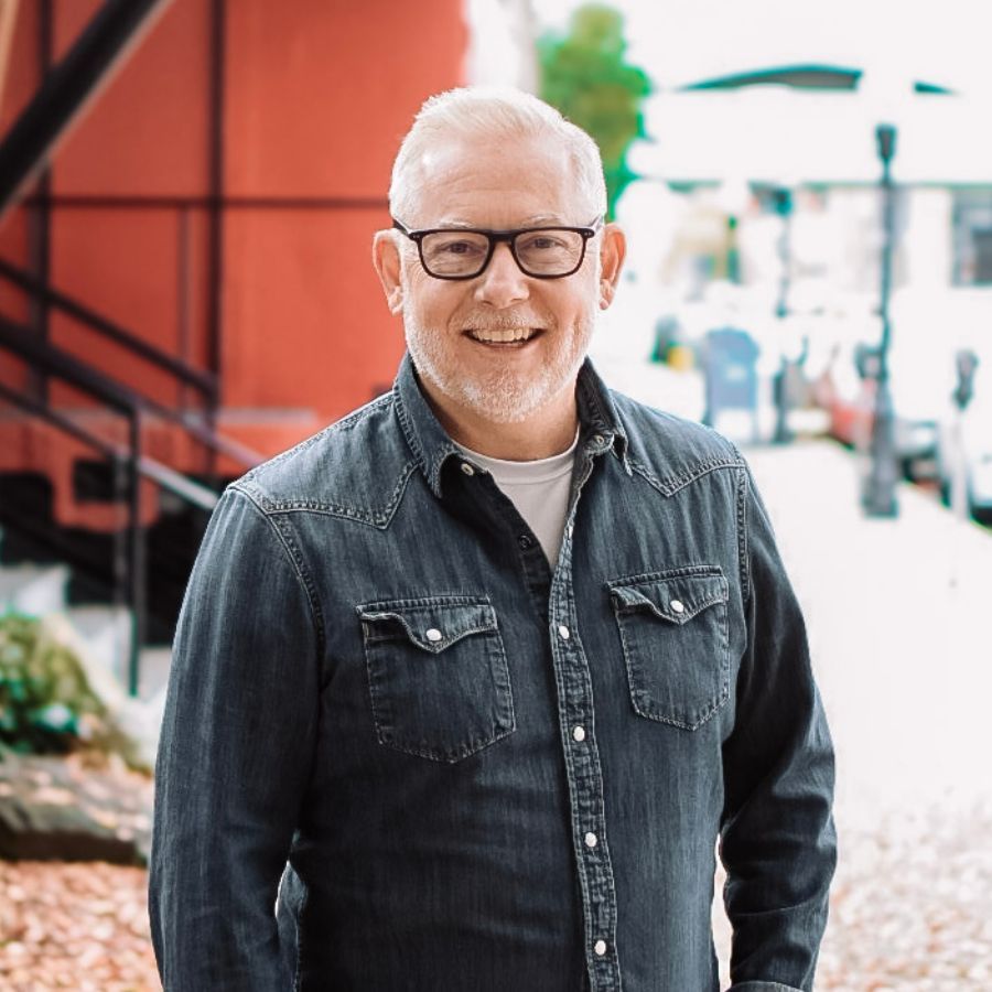 Smiling man in glasses and denim shirt standing in a bright indoor market
