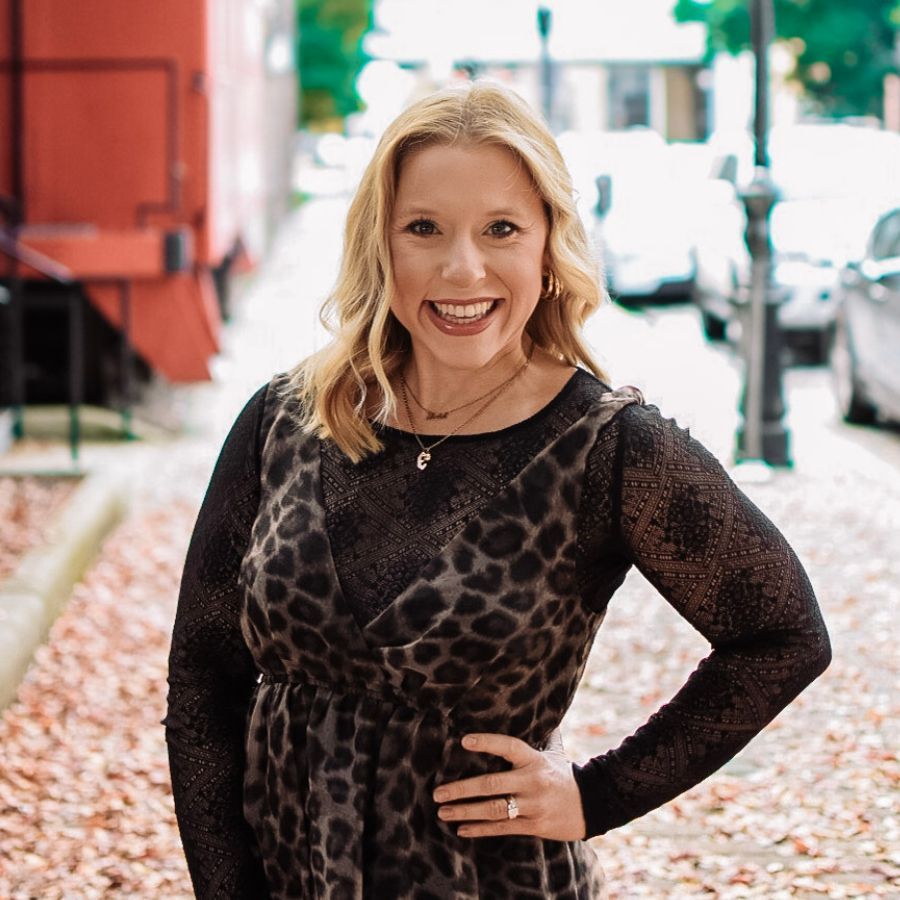 Smiling woman in a black patterned dress standing on a leaf-covered street