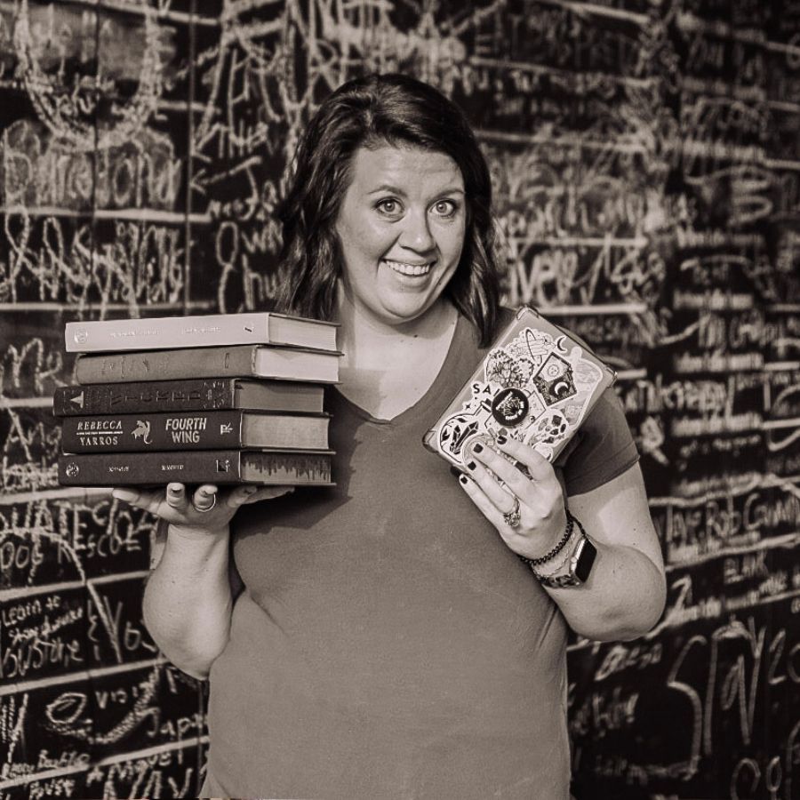 Woman holding a stack of books and a notebook in front of a chalkboard covered with writing