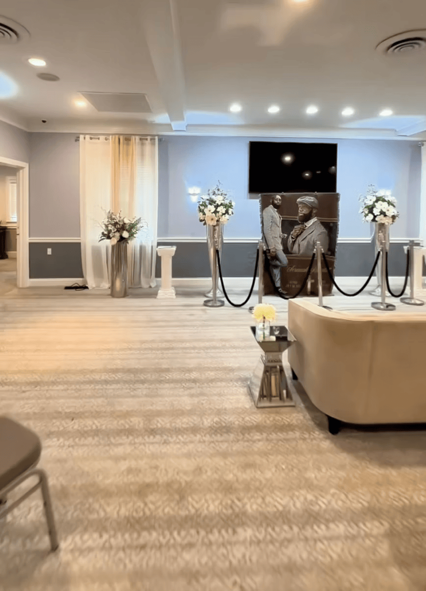 Elegant event venue with white floral arrangements, rope stanchions, and a beige sofa on a carpeted floor.
