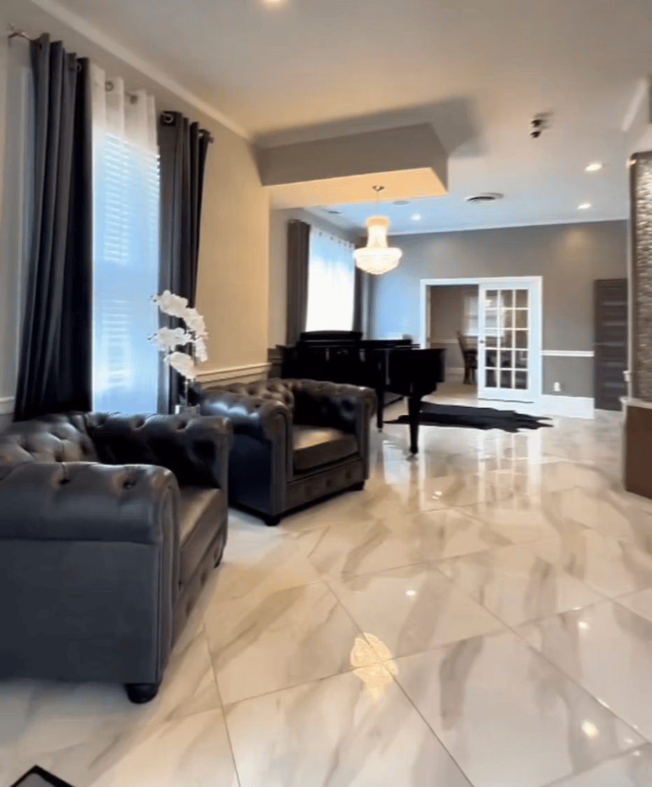 Modern living room with black leather sofas, a grand piano, and glossy marble tile floor.