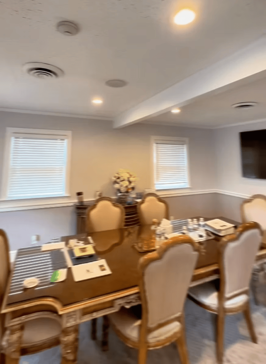Dining room with a wooden table, upholstered chairs, windows, and a wall-mounted TV.
