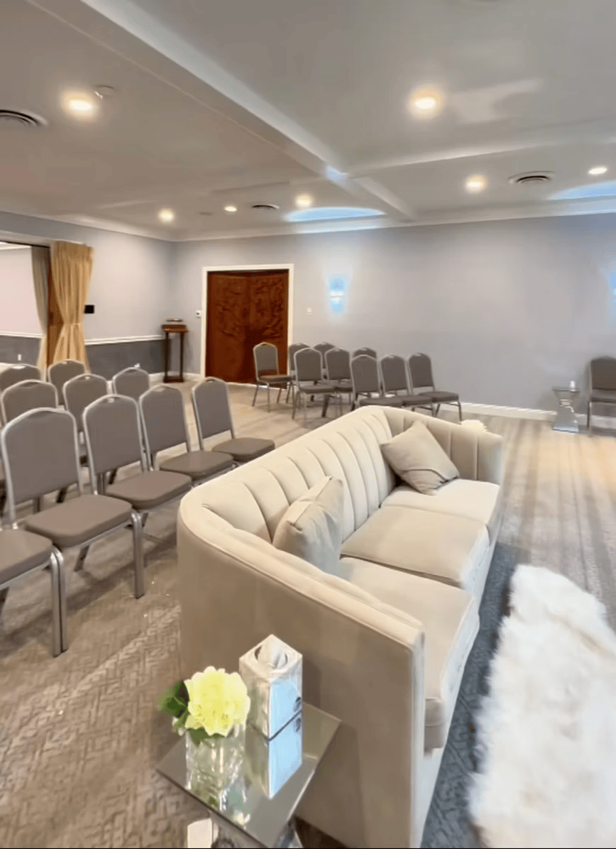 Empty event room with rows of gray chairs, a white sofa, and recessed ceiling lights