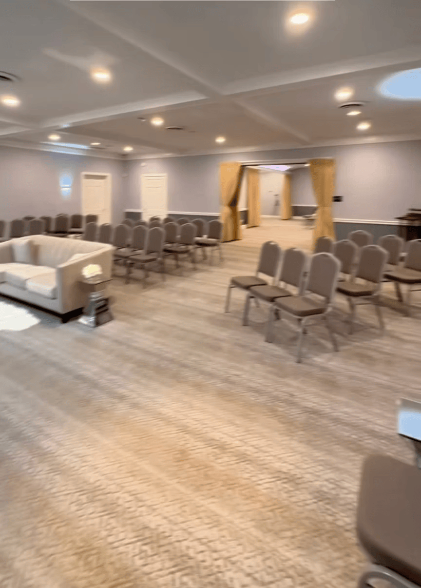 Empty conference room with rows of gray chairs, a white sofa, and recessed ceiling lights on wood flooring
