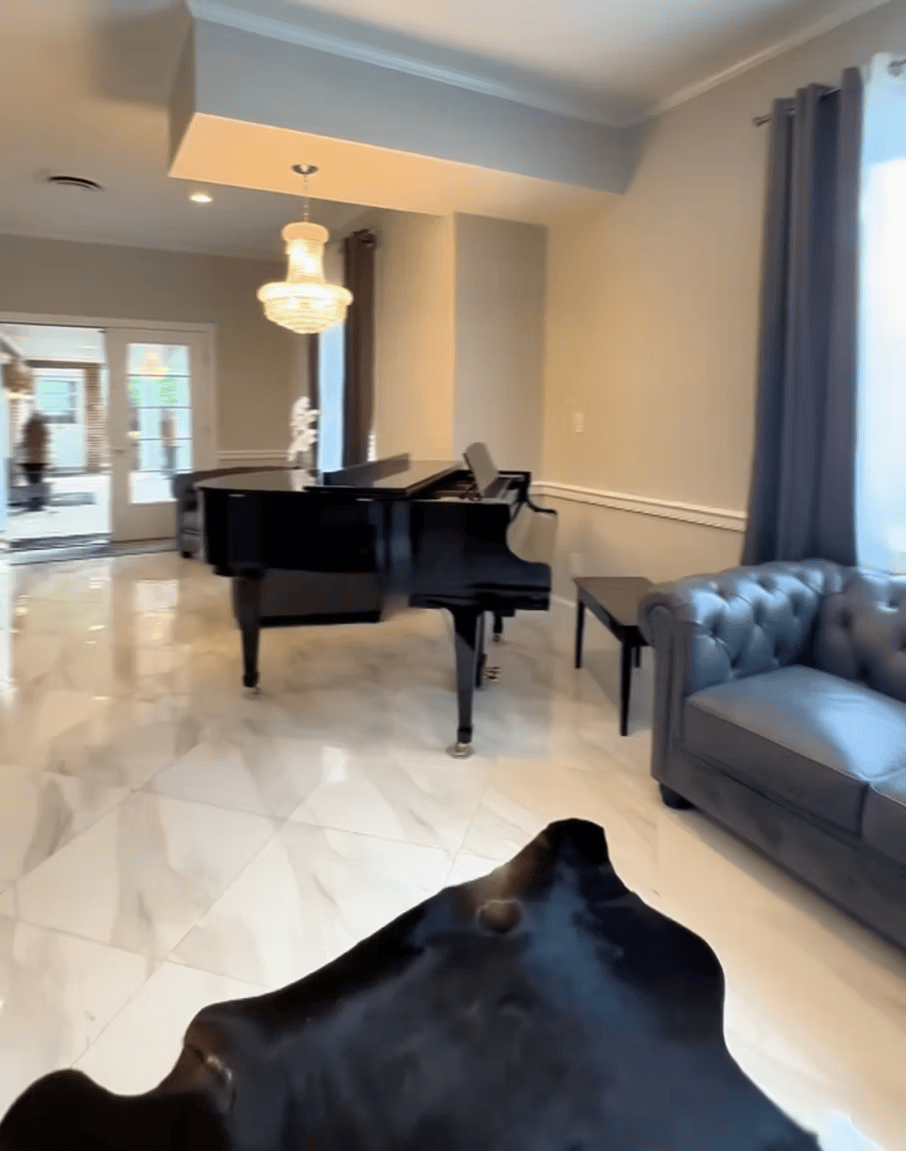 Elegant living room with black grand piano, gray sofa, chandelier, and large windows