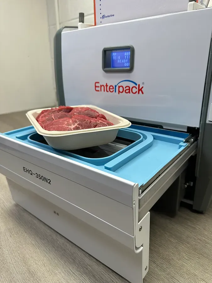 A tray of raw red meat sits on the sliding tray of a white Enterpack machine, ready to be sealed.