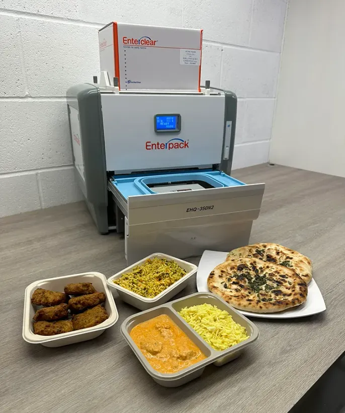 A food-sealing machine sits on a counter next to several containers of Indian-style food, including naan and curry.