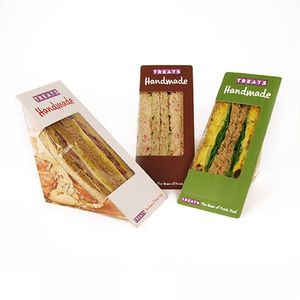 Three pre-packaged, handmade triangular sandwiches in white, brown, and green cardboard containers with viewing windows.