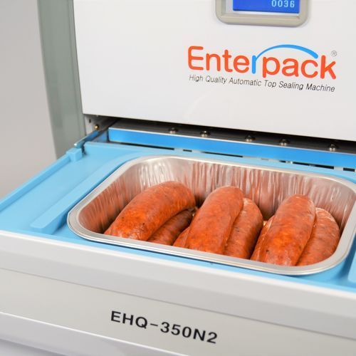 An Enterpack EHQ-350N2 automatic top sealing machine with a tray of raw sausages ready for processing.