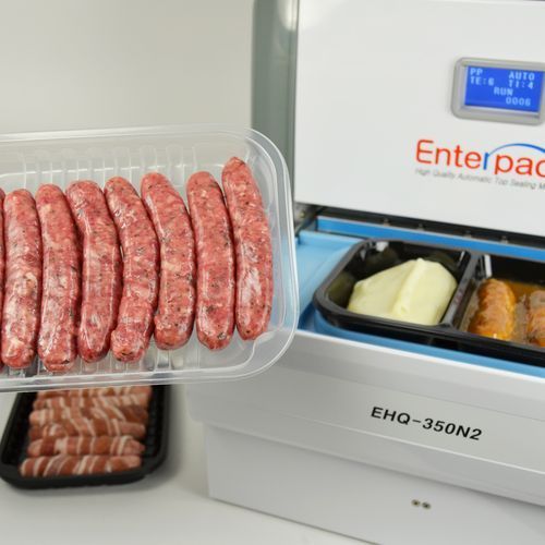 A top-sealing machine, model EHQ-350N2, sits next to trays of raw sausages and a meal tray with mashed potatoes and meat.