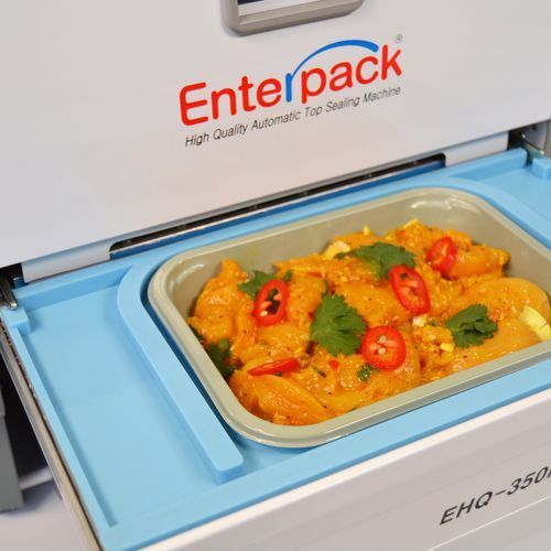 A food tray filled with curry and chili, sitting in an Enterpack top sealing machine.