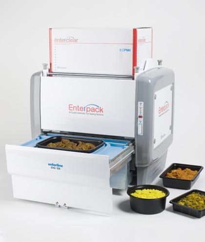 An Enterpack food tray sealing machine with a tray inserted and three other filled food containers nearby.