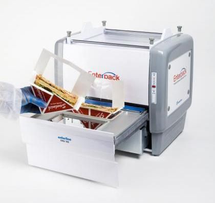 A gloved hand places a sandwich into a commercial Enterpack tray sealer machine on a white background.