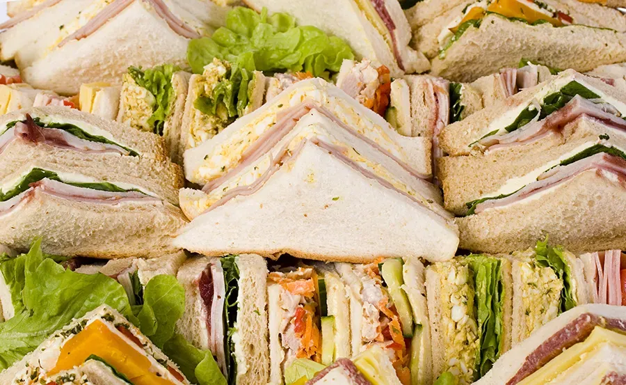 A platter filled with assorted triangle-cut sandwiches and fresh green lettuce.