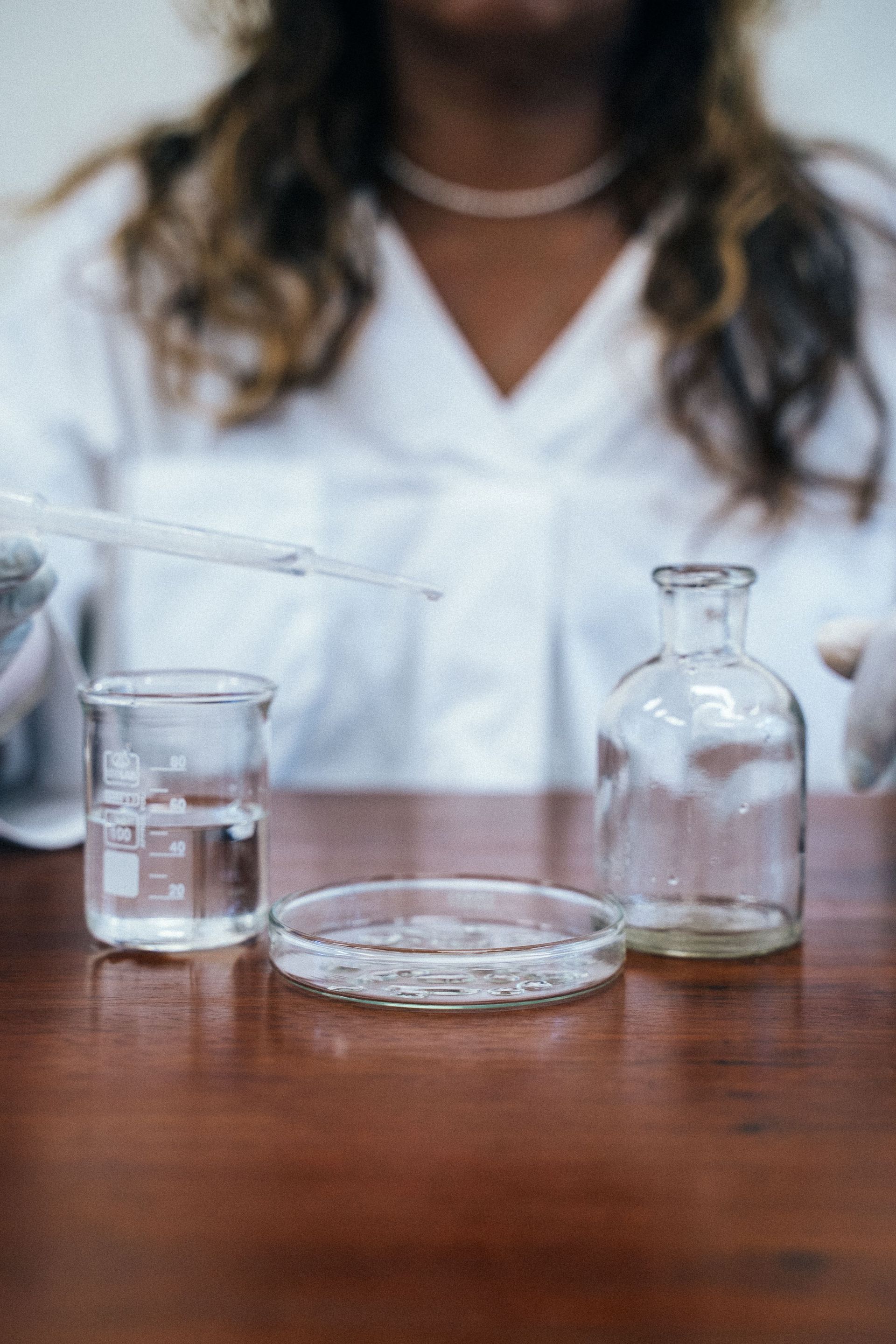 Lab glassware on a wooden table with a person in a white lab coat in the background