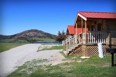 A wooden cabin with a red roof is sitting next to a lake.