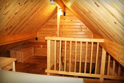 An attic in a log cabin with a wooden railing and stairs.