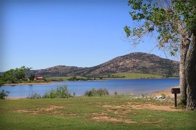 A lake with mountains in the background and a tree in the foreground.