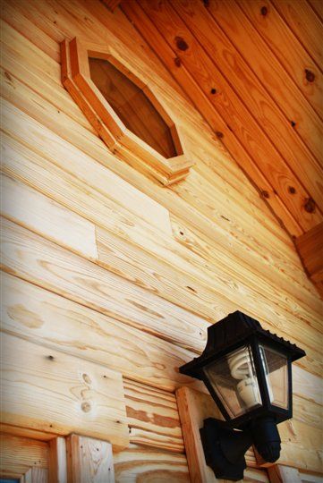A lamp is hanging on a wooden wall next to a window.
