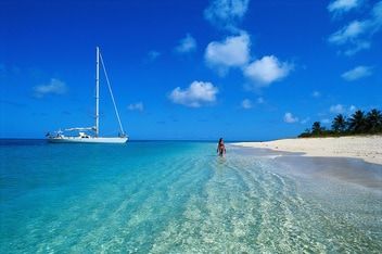 key west florida A woman is standing in the water on a beach with a sailboat in the background.