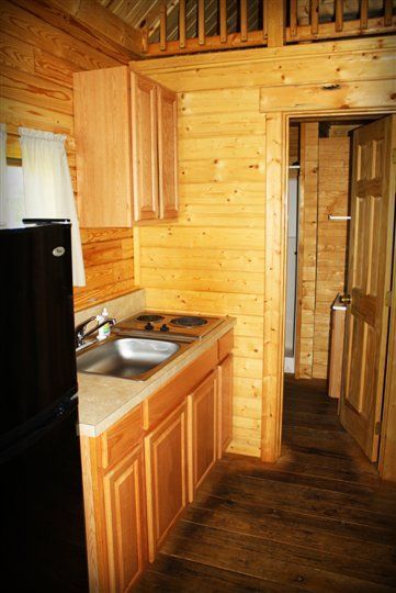 A kitchen with a sink , stove and refrigerator in a log cabin.