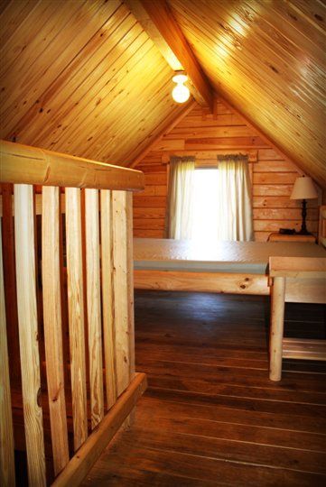 There is a bed in the attic of a log cabin.