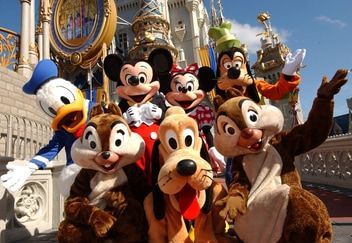 disney world A group of disney characters are posing for a picture in front of a castle.
