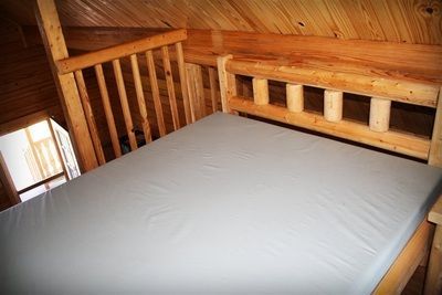 A bed in a cabin with a white mattress and a wooden railing.