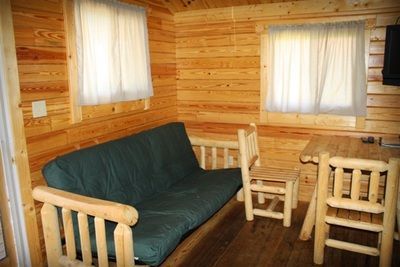 A living room in a log cabin with a futon , table and chairs.
