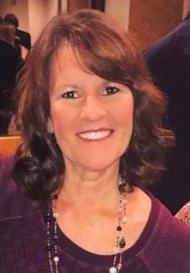 women in a purple shirt smiling A woman wearing a purple shirt and a necklace is smiling for the camera.