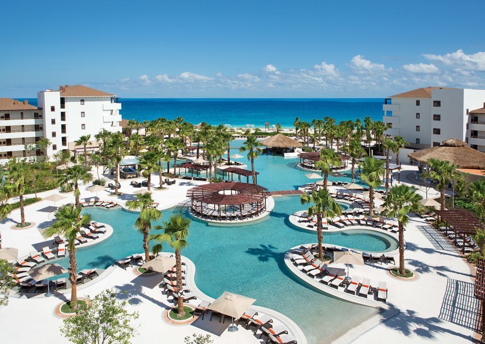 secrets playa resort An aerial view of a large swimming pool surrounded by palm trees.