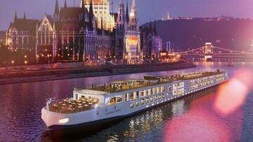 viking river cruise A cruise ship is floating on a river in front of a city at night.