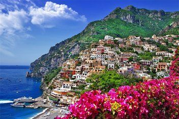 Mediterranean coastline A city on a hill overlooking the ocean with pink flowers in the foreground.