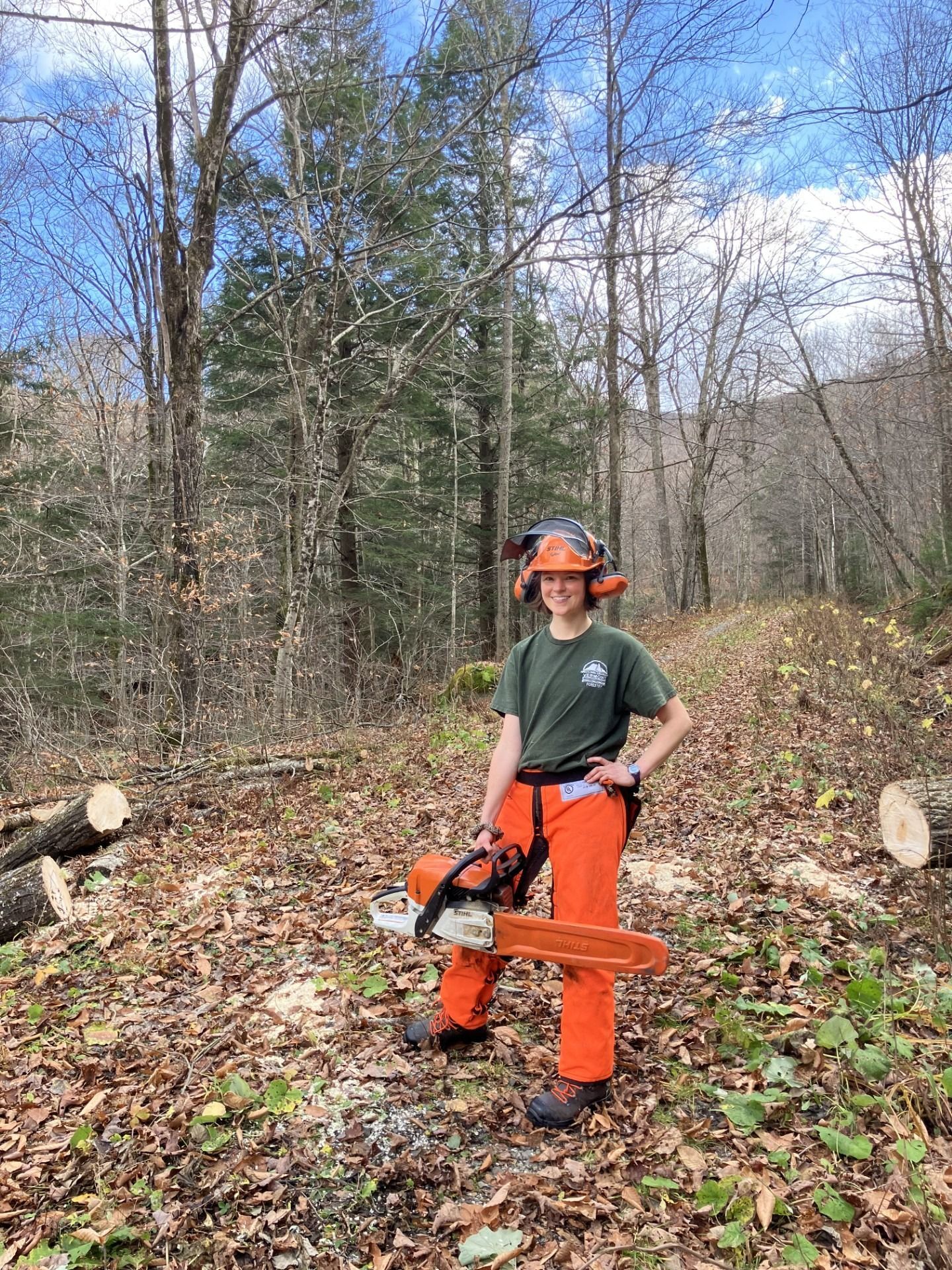 Michelle in chainsaw PPE gear, holding a chainsaw in the woods
