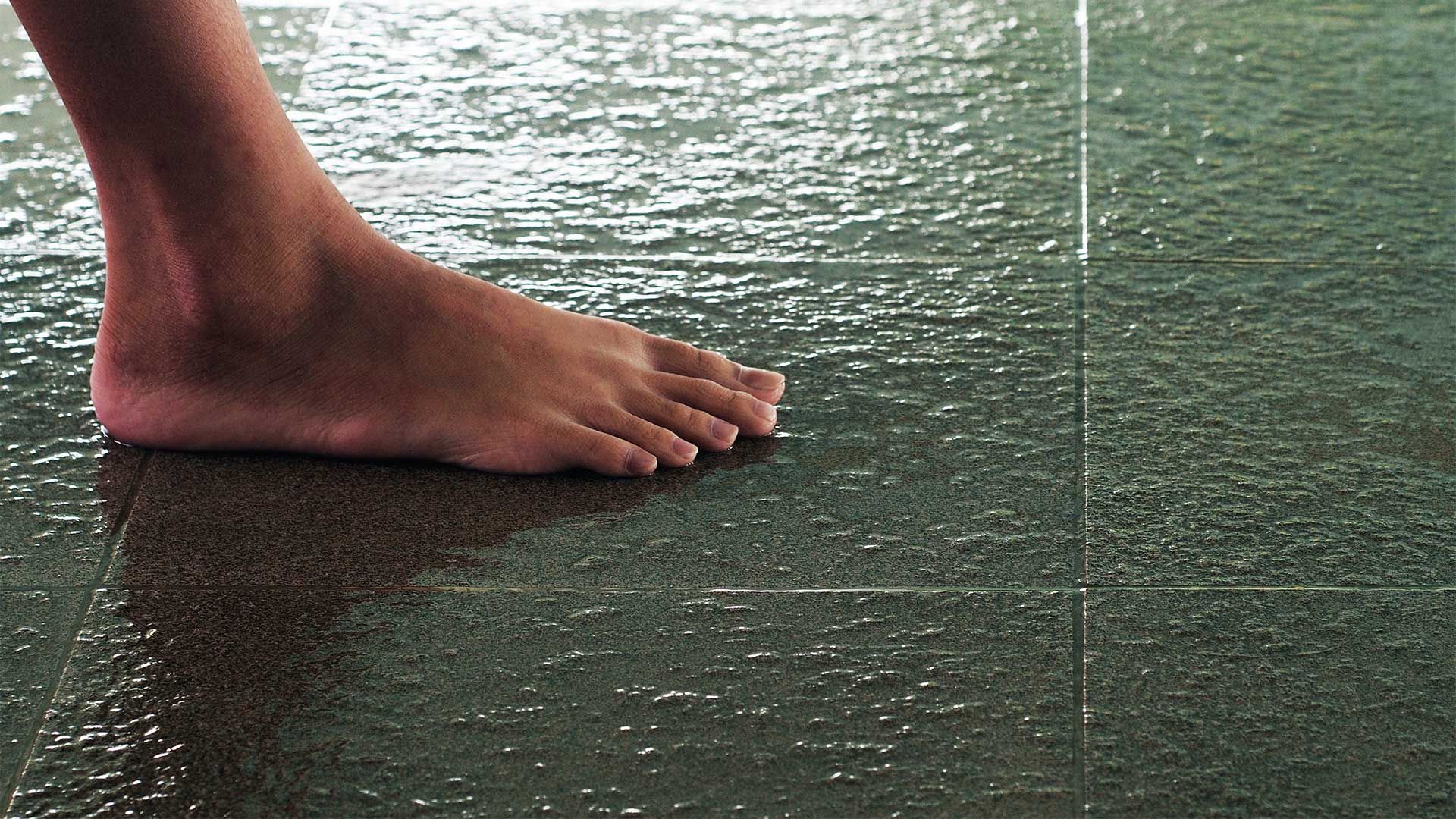 A person 's foot is standing on a wet tiled floor.