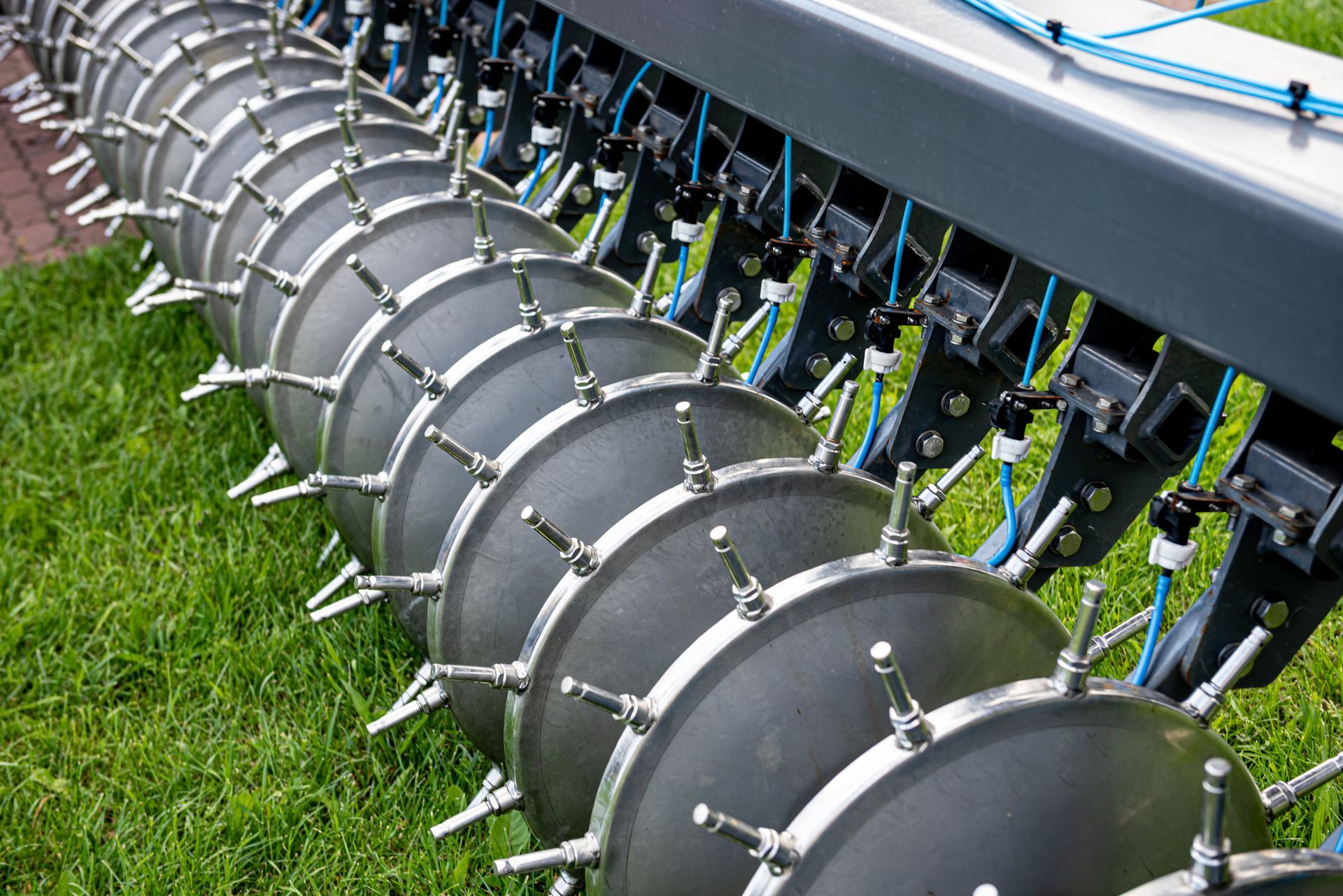 Aerator with rows of spiked wheels on a green lawn.