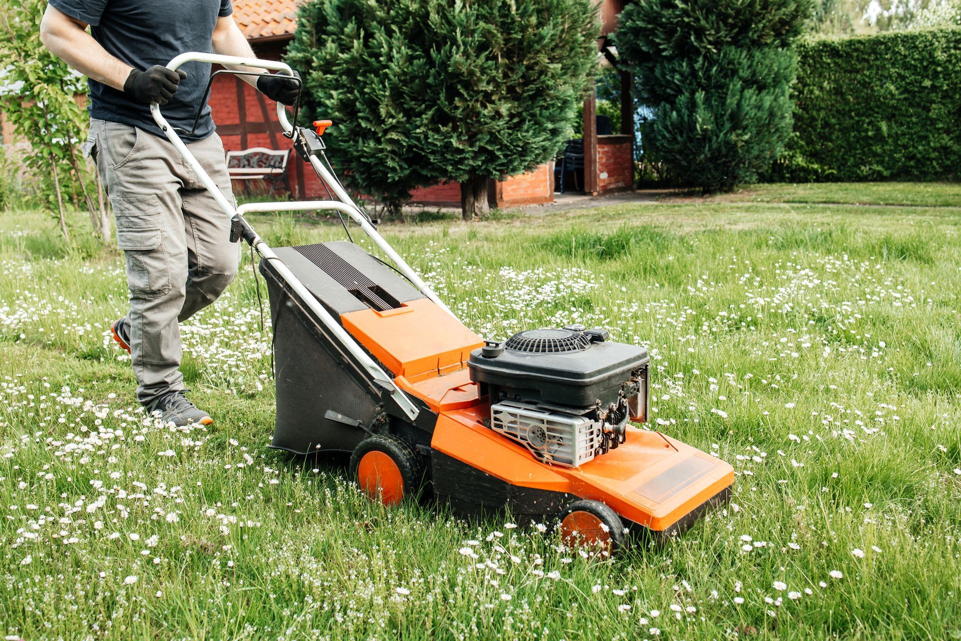 Man mowing a lawn with an orange and black lawnmower in a grassy yard.