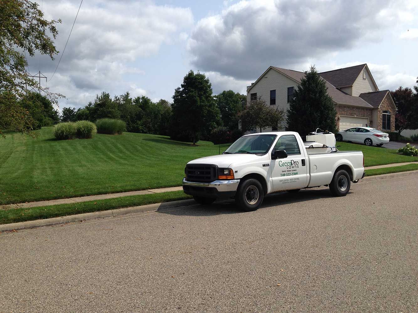 White pickup truck parked on a street, lawn care service vehicle, residential setting.