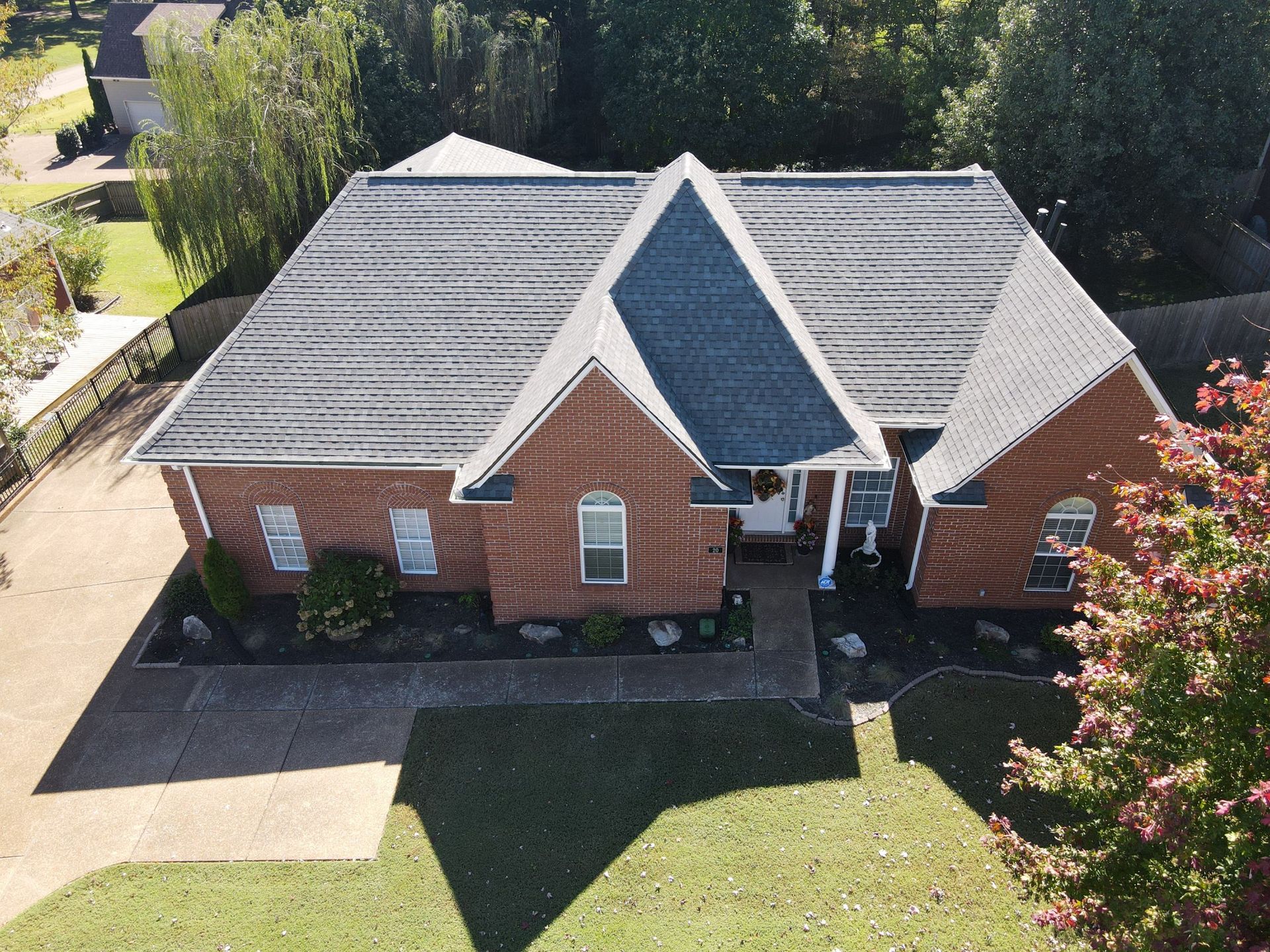 Aerial view of a brick house with a gray roof, front walkway, driveway, and green lawn.