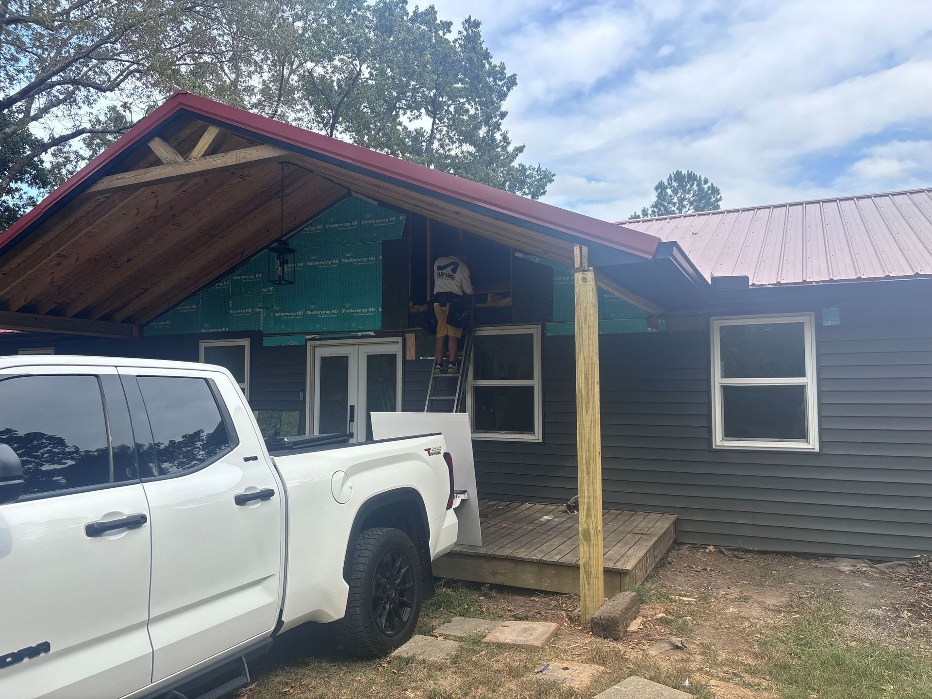 White pickup truck parked beside a small house with a red roof and covered porch.