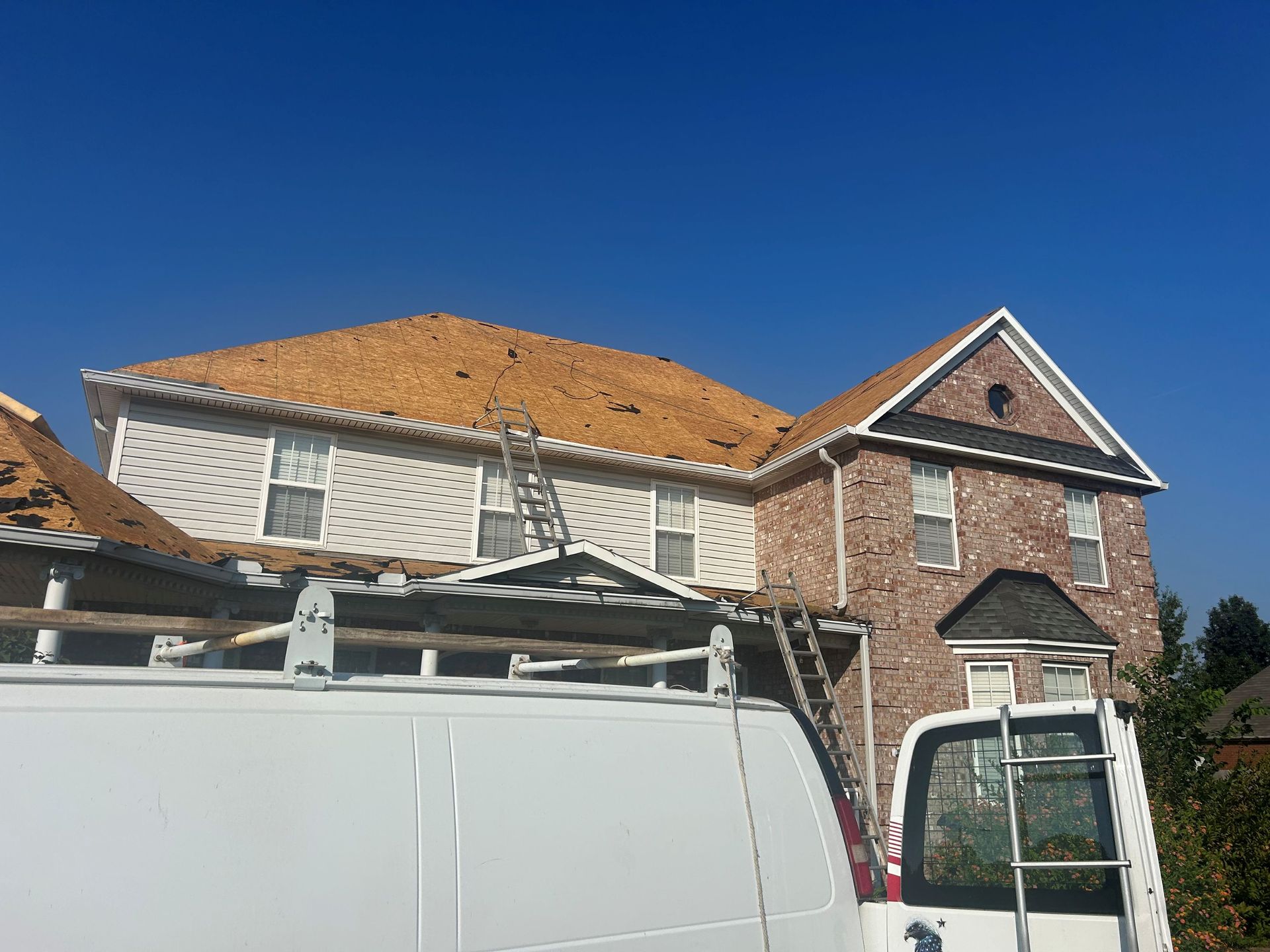 Brick house with damaged roof and scaffolding behind a white van under a clear blue sky