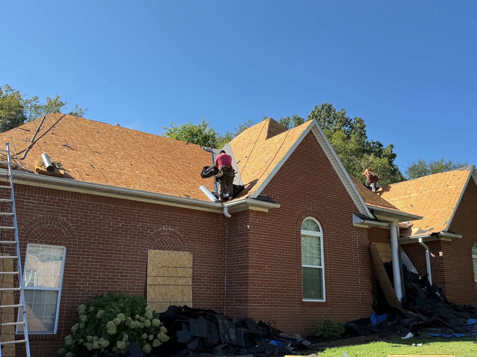 Roofers repairing a red brick church roof under a clear blue sky