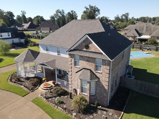 Aerial view of a two-story brick house with a gray roof, landscaped yard, and backyard gazebo.