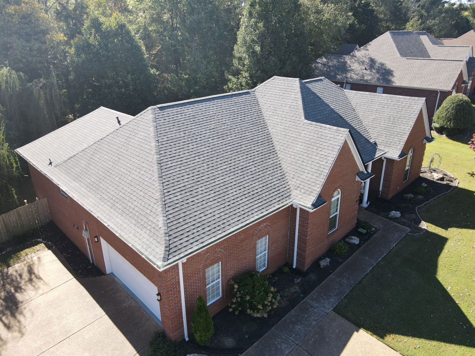 Aerial view of several red-brick houses with light gray roofs and green lawns in a residential neighborhood