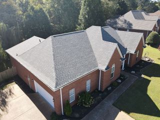 Aerial view of two red-brick houses with light gray roofs beside a green lawn and trees.