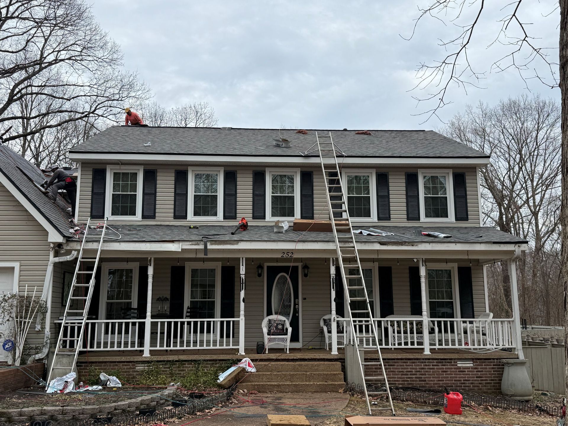 Two-story gray house with white trim and wraparound porch decorated for the holidays
