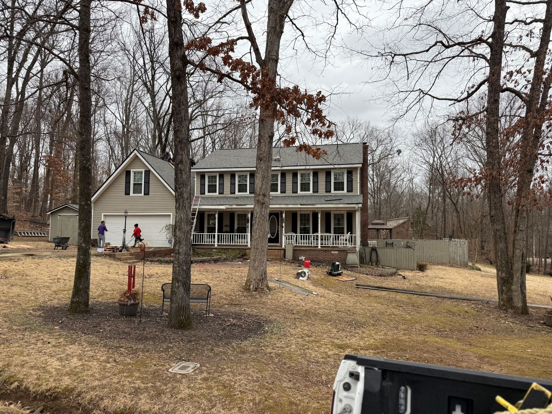 Rural house with porch and bare trees in winter, with a few people in the yard